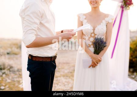Sibenik, Kroatien - 05.06.17: Der Bräutigam hält ein Blatt Papier vor sich. Lächelnde Braut mit Lavendel-Bouquet steht in der Nähe. Nahaufnahme Stockfoto