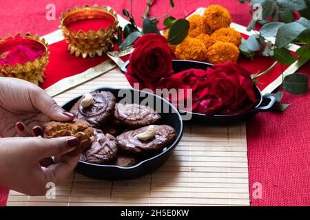 Hände weiblicher Mädchen halten gebrochene Stücke von populären trockenen süßen Dessert Indian Thekua Khajoor während Chhath Puja Anbetung oder Holi Feiern gekocht W Stockfoto
