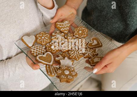 Weihnachts-Ingwerkekse, die in den Händen von Mutter und Tochter mit Puderzucker auf einer Glasplatte dekoriert sind Stockfoto