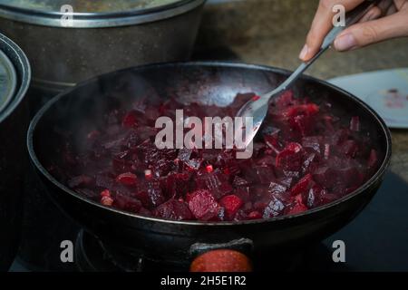 Nahaufnahme der Hand einer Frau, die in Würfel geschnittene Rüben, Karotten und Knoblauch in einer Pfanne mischt Stockfoto