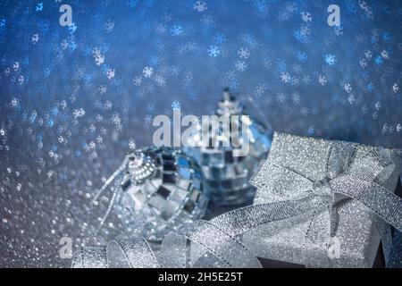 Blauer festlicher Сhristmas-Hintergrund mit Bokeh in Form von Schneeflocken, Geschenkbox und glänzenden Kugeln. Selektiver Fokus, freier Platz für Text. Stockfoto