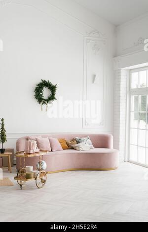 Rosa Sofa in einem weißen Wohnzimmer dekoriert für Weihnachten und Neujahr. Ein Kranz an der Wand über dem Sofa Stockfoto