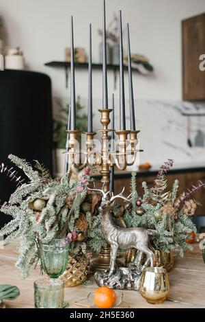 Festliches weihnachtliches Dinner. Hirsch-Souvenir, Kerzen im Kerzenständer, Gläser, Mandarine und Zweige von Tanne oder Fichte in einer Vase Stockfoto