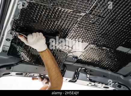 Arbeiter klebt Schalldämmmaterial auf die Innenseite des Autodachs. Prozess der Installation der Schalldämmung im Auto. Stockfoto