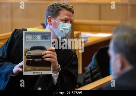 Aachen, Deutschland. November 2021. Der Verteidiger Sören Gemmerich (M) sitzt neben einem Angeklagten (nicht abgebildet) im Dock des Landgerichts Aachen und zeigt seinen Mitanwälten in einem Porsche-Magazin etwas. Drei Männer wurden vor dem Landgericht angeklagt, historische Rennwagen nachgebaut und gefälschte Dokumente an das Genehmigungsamt für den Straßenverkehr geschickt zu haben. Quelle: Marius Becker/dpa/Alamy Live News Stockfoto