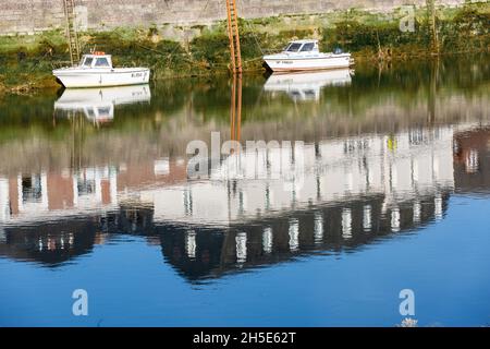 Kleine Fischerboote, die bei Ebbe vor Anker liegen. Spiegelungen von Häusern, die am Kai gebaut wurden. Saint-Valery, Somme-Bucht, Frankreich Stockfoto