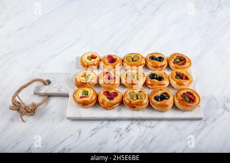 Mini Hot Dogs werden als offenes Buffet serviert. Mini-Pizzas mit Gemüse, Mozzarella-Käse und frischem Basilikum auf Marmorboden, Nahaufnahme, Draufsicht. Stockfoto