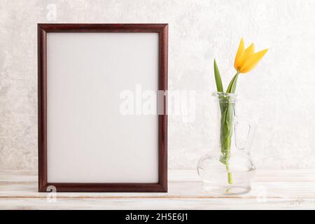 Holzrahmen mit orangefarbener Tulpenblume in Glas auf grauem Betongrund. Seitenansicht, Kopierraum, Stillleben, Mockup, Schablone, Frühling, Sommer Minima Stockfoto