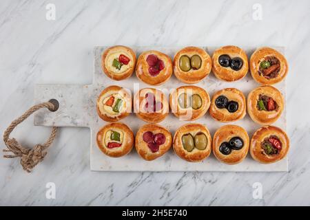 Mini Hot Dogs werden als offenes Buffet serviert. Mini-Pizzas mit Gemüse, Mozzarella-Käse und frischem Basilikum auf Marmorboden, Nahaufnahme, Draufsicht. Stockfoto