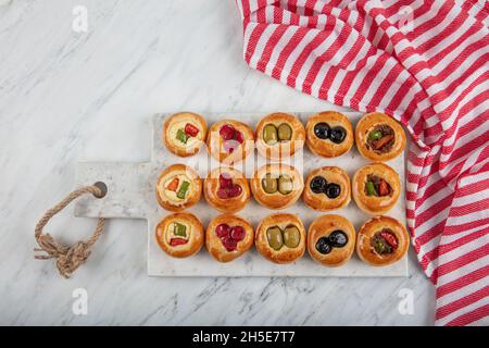 Mini Hot Dogs werden als offenes Buffet serviert. Mini-Pizzas mit Gemüse, Mozzarella-Käse und frischem Basilikum auf Marmorboden, Nahaufnahme, Draufsicht. Stockfoto