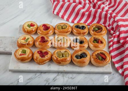 Mini Hot Dogs werden als offenes Buffet serviert. Mini-Pizzas mit Gemüse, Mozzarella-Käse und frischem Basilikum auf Marmorboden, Nahaufnahme, Draufsicht. Stockfoto