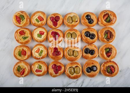 Mini Hot Dogs werden als offenes Buffet serviert. Mini-Pizzas mit Gemüse, Mozzarella-Käse und frischem Basilikum auf Marmorboden, Nahaufnahme, Draufsicht. Stockfoto