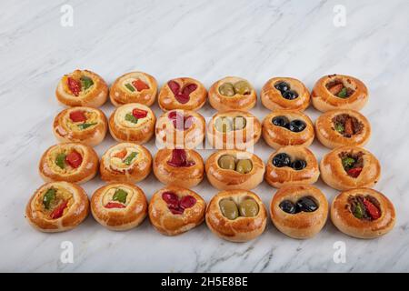 Mini Hot Dogs werden als offenes Buffet serviert. Mini-Pizzas mit Gemüse, Mozzarella-Käse und frischem Basilikum auf Marmorboden, Nahaufnahme, Draufsicht. Stockfoto