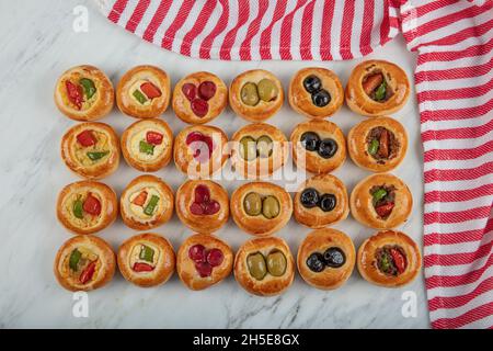 Mini Hot Dogs werden als offenes Buffet serviert. Mini-Pizzas mit Gemüse, Mozzarella-Käse und frischem Basilikum auf Marmorboden, Nahaufnahme, Draufsicht. Stockfoto