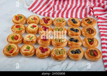 Mini Hot Dogs werden als offenes Buffet serviert. Mini-Pizzas mit Gemüse, Mozzarella-Käse und frischem Basilikum auf Marmorboden, Nahaufnahme, Draufsicht. Stockfoto