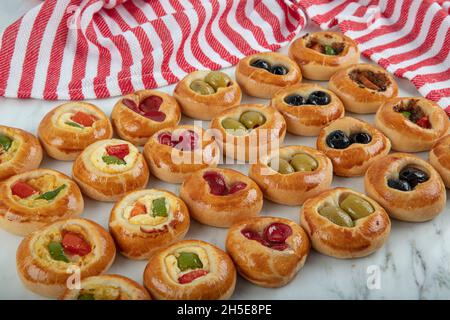 Mini Hot Dogs werden als offenes Buffet serviert. Mini-Pizzas mit Gemüse, Mozzarella-Käse und frischem Basilikum auf Marmorboden, Nahaufnahme, Draufsicht. Stockfoto