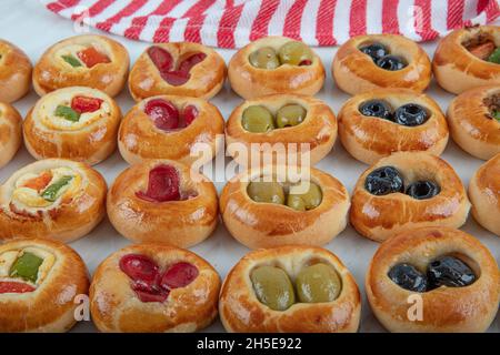 Mini Hot Dogs werden als offenes Buffet serviert. Mini-Pizzas mit Gemüse, Mozzarella-Käse und frischem Basilikum auf Marmorboden, Nahaufnahme, Draufsicht. Stockfoto