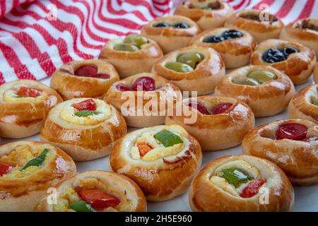 Mini Hot Dogs werden als offenes Buffet serviert. Mini-Pizzas mit Gemüse, Mozzarella-Käse und frischem Basilikum auf Marmorboden, Nahaufnahme, Draufsicht. Stockfoto