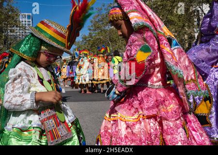 Barcelona, Spanien - Hispanic Day, 2021: Zwei ethnische bolivianische Mädchen überprüfen ihre traditionellen Kostüme, bevor sie durch die Straßen der Stadt ziehen. Stockfoto