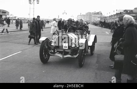 In den 1980er Jahren, historisch, ein Mann mit Hut und Stacheln und eine Frau mit Mantel und Kopftuch in einem Veteranenwagen (Nr. 234) im Ziel des berühmten London to Brighton Veteran Car Run, Brighton, W. Sussex, England, Großbritannien. Es ist die am längsten laufende Motorveranstaltung der Welt, die erste Ausgabe fand 1896 statt. Um sich für die Teilnahme zu qualifizieren, müssen Autos vor 1905 gebaut worden sein. Stockfoto