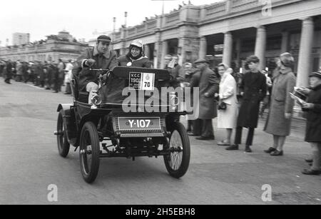 80er Jahre, historisch, ein Oldtimer - Y-107 - mit einem Mann, der fährt, und einer weiblichen Passantin, am Ziel des Veteran Car Run von London nach Brighton, Brighton, W. Sussex, England, Großbritannien. Es ist die am längsten laufende Motorveranstaltung der Welt, die erste Ausgabe fand 1896 statt. Um sich für die Veranstaltung zu qualifizieren, müssen Autos vor 1905 gebaut worden sein. Stockfoto