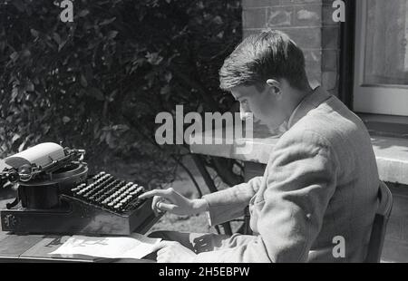 1937, historisch, sommerlich und außerhalb eines Hauses, könnte ein junger Mann in einer Jacke, der mit einer Schreibmaschine an einem Tisch sitzt, England, Großbritannien, ein Student einen College-Auftrag schreiben. Die Schreibmaschinen, die Anfang der 1870er Jahre kommerziell eingeführt wurden, wurden zu einem unverzichtbaren Werkzeug für alle Schreibarten, sowohl im geschäftlichen als auch im privaten Bereich und blieben bis in die 1980er Jahre eine Standardschreibmaschine in den meisten Büros, bis sie vom PC durch Textverarbeitungssoftware ersetzt wurden. Stockfoto