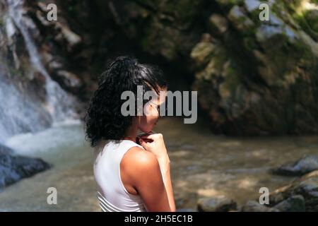 Junge Frau, die bei einem Wasserfall steht. Urlaub und Tourismus Konzept Stockfoto