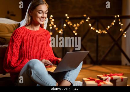 Weihnachtsgeschäfte. Lächelnde Dame, die mit einem Laptop Geschenke auswählt Stockfoto