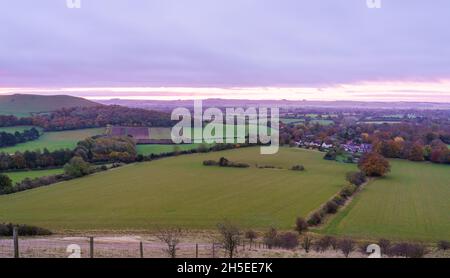 Wunderschöne Sonnenaufgangsszenerie mit Blick auf die Dorfanlage von Oare vom südseitigen Rand der Marlborough Downs, neben Pewsey Val, Wiltshire AON Stockfoto