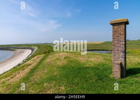 Panoramablick über den Deich bei Oosterend auf der niederländischen Insel Texel mit Strand, Feuchtgebieten und im Vordergrund ein gemauertes Denkmal, Stockfoto