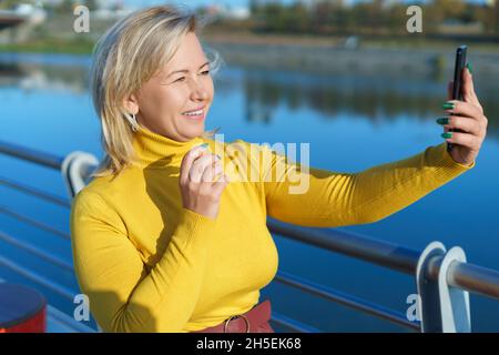 Lächelnde kaukasische Frau mittleren Alters, die am Flussufer per Video telefoniert. Stockfoto