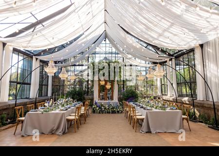 Hochzeitssaal im Gewächshaus, Tische sind gedeckt, dekoriert mit frischen Blumen, Kerzen und Kristallleuchtern. Weicher, selektiver Fokus. Stockfoto