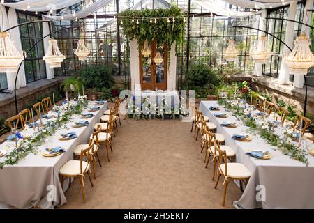 Hochzeitssaal im Gewächshaus, Tische sind gedeckt, dekoriert mit frischen Blumen, Kerzen und Kristallleuchtern. Weicher, selektiver Fokus. Stockfoto