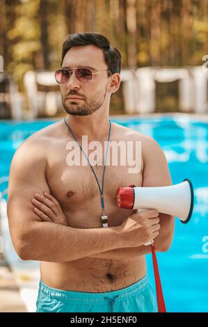 Männlicher Rettungsschwimmer mit Sonnenbrille in der Nähe des öffentlichen Schwimmbades Stockfoto