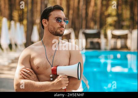 Männlicher Rettungsschwimmer mit Sonnenbrille in der Nähe des öffentlichen Schwimmbades Stockfoto