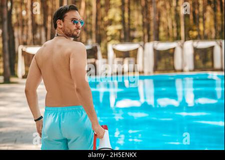 Ein Rettungsschwimmer in blauen Shorts, der in der Nähe des Pools steht Stockfoto