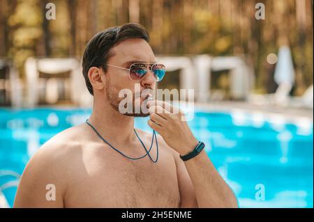 Männlicher Rettungsschwimmer mit Sonnenbrille in der Nähe des öffentlichen Schwimmbades Stockfoto