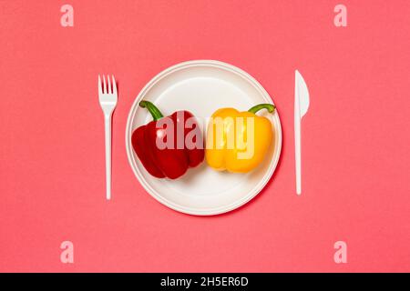 Rote und gelbe Paprika auf einem weißen Teller, Gabel und Messer, Diät, gesunde Ernährung Konzept. Kreatives Lebensmittelkonzept. Draufsicht Rosa Hintergrund flach lag w Stockfoto