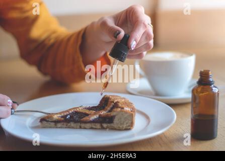 Ein Mädchen in einer gelben Jacke frühstückt in einem Café. Damenhänden fügen THC und CBD-Öl zum Kirschkuchen hinzu. Das Konzept der Verwendung von medizinischem Marihuana. Stockfoto