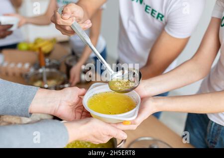 Freiwillige, die heiße Suppe für Obdachlose im gemeinnützigen Spendenzentrum der Gemeinde servieren, eine Gruppe junger Menschen, die mit Essen helfen Stockfoto