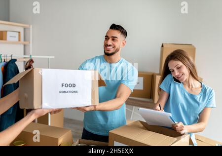 Glückliche Freiwillige, die Lebensmittelspenden in Kartons sortieren und verpacken, Frau, die im Clipboard schreibt Stockfoto