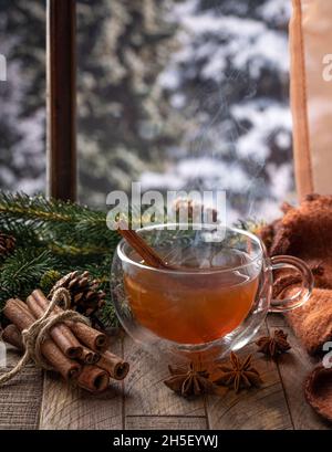 Dampfende heiße Tasse Tee auf einem Holztisch an einem Fenster mit Winterhintergrund Stockfoto