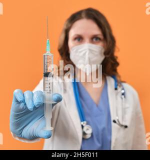 Ärztin hält Spritzen in der Hand auf einem roten Hintergrund, Konzept. Krankenschwester mit Spritzen zur Injektion gegen Coronavirus Stockfoto