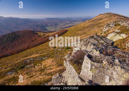 Blick auf die Hügel mit Wasserscheidekamm, bedeckt mit rotem, orangefarbenem und gelbem Laubwald und grünen Kiefern unter blauem Himmel am warmen Herbsttag in Octob Stockfoto