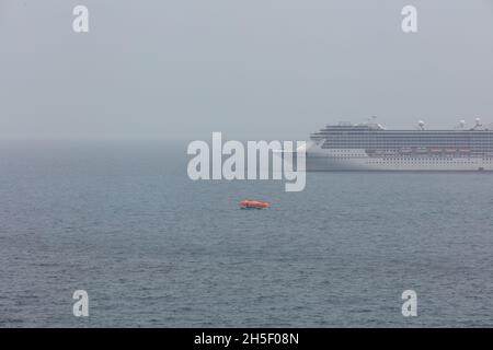 Das Karibische Meer - 26. Mai 2020: Luftaufnahme von Carnival Pride vor Anker auf dem Meer und ein einziges Rettungsboot vor ihr. Grauer, nebliger Himmel im b Stockfoto