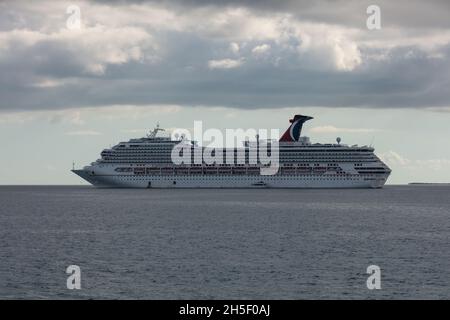 Belize Coast - 1. Januar 2020: Luftaufnahme der Carnival Conquest vor der Küste von Belize und ein kleines zartes Boot von ihr verankert. Blauer Himmel und weißer c Stockfoto