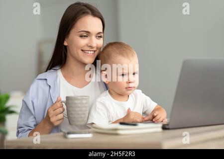 Technologie Und Kinderbetreuung. Mutter Trinkt Tee, Während Baby Beobachten Cartoons Auf Laptop Stockfoto