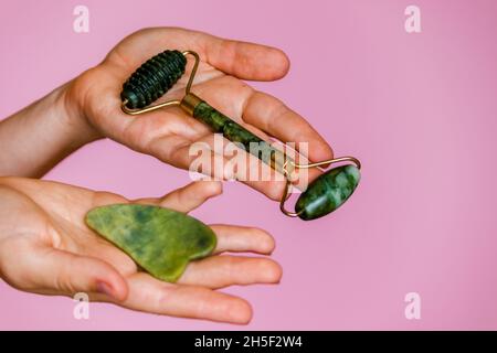 Jade Roller und Scruber für Gesichtsmassage in weiblichen Händen auf einem rosa Hintergrund. Stockfoto