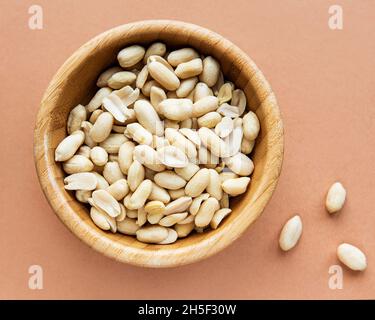 Geschälte Erdnüsse in einer Holzschale auf braunem Hintergrund Stockfoto