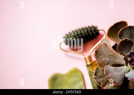 Jade Roller und Gesichtsmassage Scrubber auf einem weichen rosa Hintergrund. Stockfoto